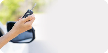 A hand is holding a car key, with the sideview mirror of the car in the background.