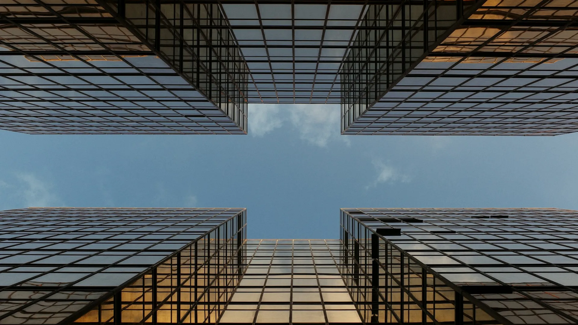 A worm view photo of a building with glass walls under a partly cloudy blue sky.